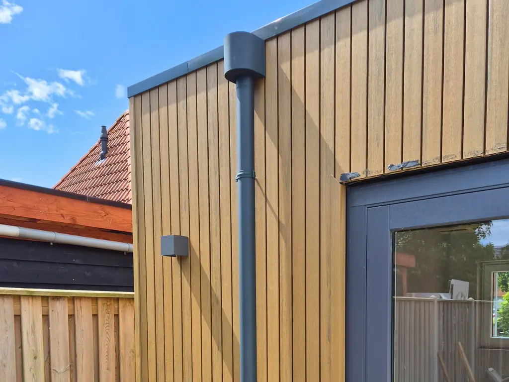 Antraciet aluminium regenpijp met vergaarbak tegen een houten gevel